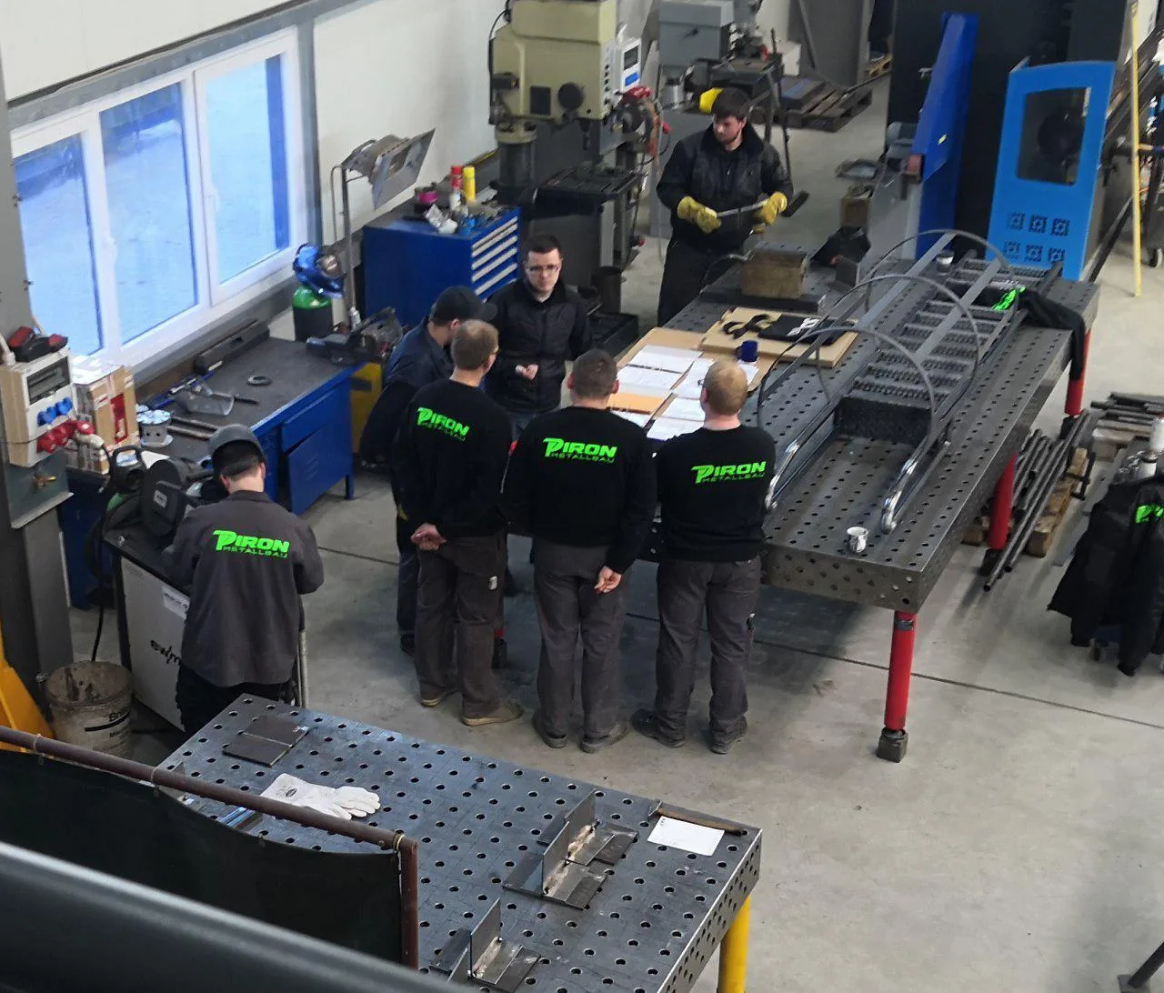 Pracownicy PIRON Metallbau GmbH omawiają rysunek techniczny przy stole warsztatowym